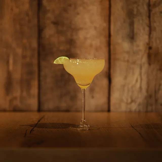 Margarita op de houten toog van AXXES: gele cocktail in een margaritaglas met een schijfje limoen