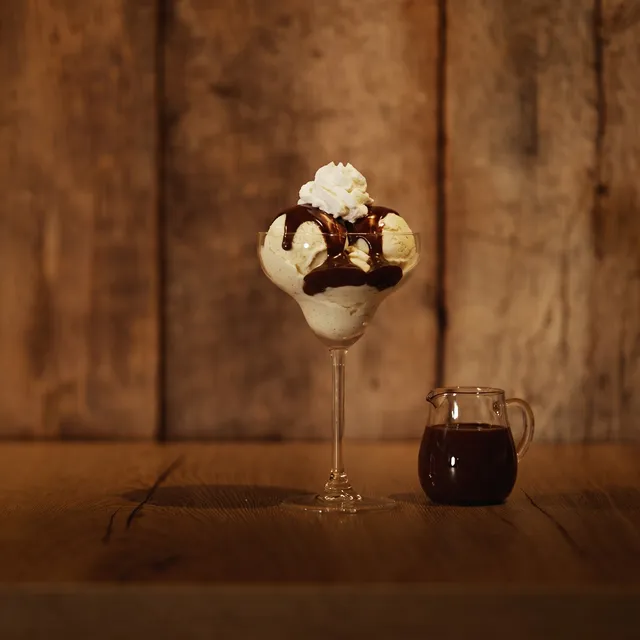 Dame blanche op de houten toog: vanille-ijs met warme chocoladesaus en slagroom, met een kannetje chocoladesaus